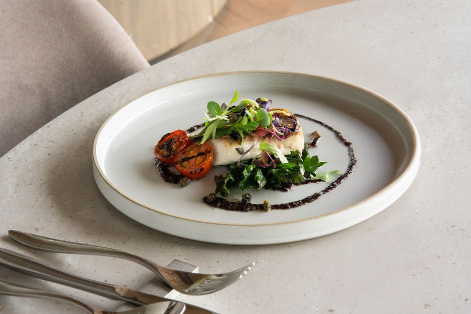 Delicate gourmet dish featuring grilled tomatoes and greens on a white plate