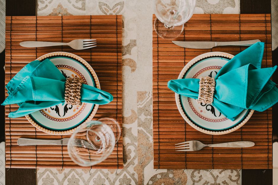 Top view stylish arrangement of ornamental plates with blue napkins served on place mat on table near wineglasses